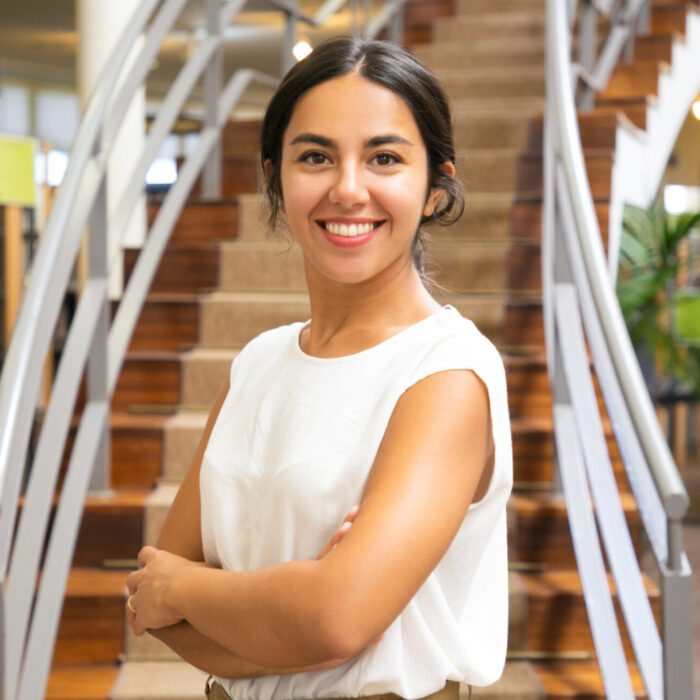 Beautiful Asian woman posing at library. Front view of smiling lady with crossed arms posing in front of stairs. Knowledge concept